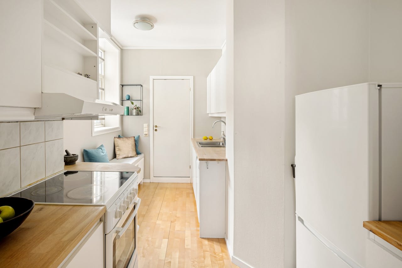 Modern white kitchen with wooden floors and minimalistic design, featuring a cozy seating area.