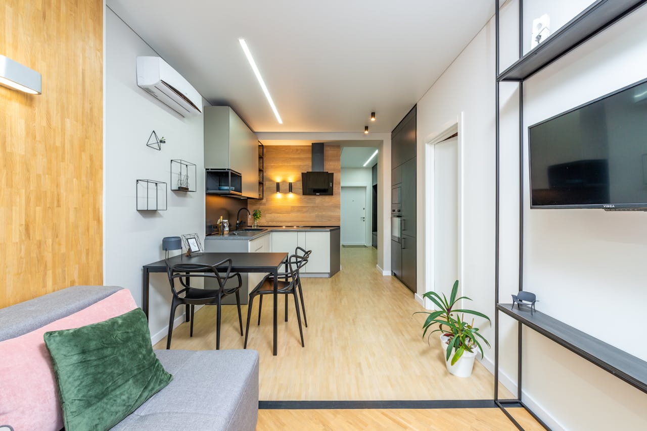 Spacious studio apartment with sofa and TV set in living room and comfortable kitchen with modern appliances and table with chairs